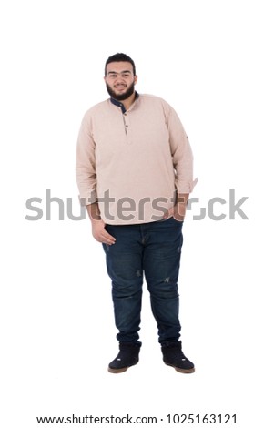 A full-length shot of an unfitness young man standing hands in pocket wearing a shirt and jeans, isolated on a white background. Royalty-Free Stock Photo #1025163121
