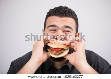 An unfitness man takes a bite of a burger sandwich with closed eyes. Royalty-Free Stock Photo #1025163277