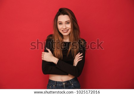 Photo of cute young woman standing isolated over red background. Looking camera.