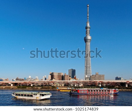 Sightseeing boats cruising on Sumidagawa River on a beautiful sunny day and the landmark Tokyo Skytree Tower standing out among modern buildings under blue clear sky, viewed from Asakusa, Tokyo, Japan Royalty-Free Stock Photo #1025174839
