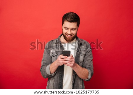 Picture of Smiling bearded man writing message on smartphone over red background