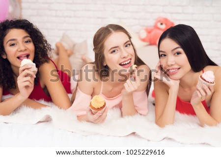 Three girls in white and red dresses lying on bed with cupcakes. They are celebrating women's day March 8.