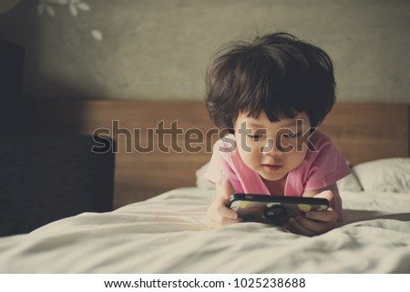 Asian Chinese girl playing smartphone on bed. watching smartphone. kid use phone and play game. child use mobile. addicted game and cartoon
