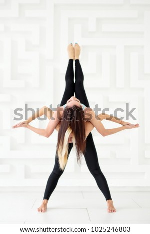 Young women practicing balance pose over a white wall. Sporty women doing acro yoga together
