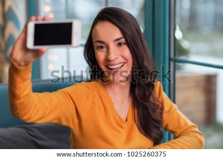 Nice shot. Happy vigorous enthusiastic woman carrying phone while posing for selfie and grinning