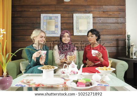 Multi race girls eating cookies,drink tea,smile,laughing and enjoy the Aidilfitri Feast Celebration.Beautiful girls wearing traditional Malaysian dress during Aidilfitri feast.