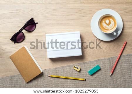 Blank white lightbox with copy space for writing a message lying on office desk with notebook as flat lay from bird's eye view