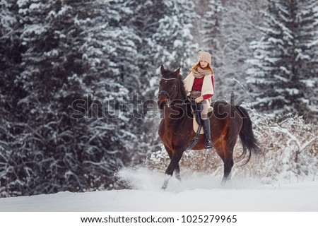 Close-up of girl rider riding horse through winter forest.