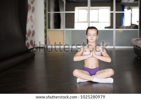 little caucasian girl sitting on mat in yoga pose and meditating