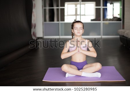 little caucasian girl sitting on mat in yoga pose and meditating