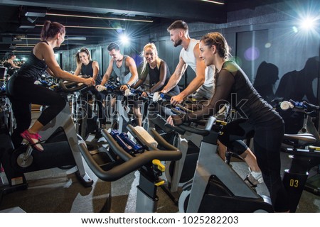 Group of attractive women and men pedaling on a stationary bikes at the gym. Royalty-Free Stock Photo #1025282203