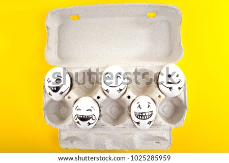 Easter eggs with drawn cartoon faces in a cardboard tray on yellow background.