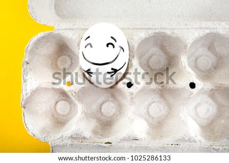 Easter egg with funny face in a cardboard tray on yellow background. Close up.