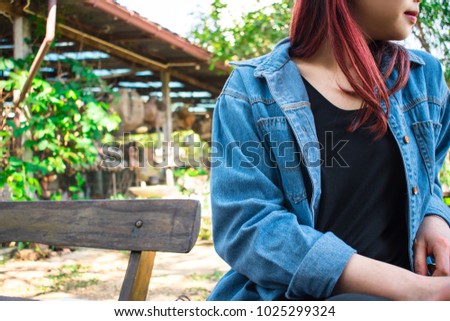 Women wear black t-shirt and blue shirt. Sit on a wooden chair facing left. Thailand, Asia
