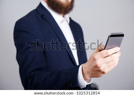 Man's hand wearing suit showing a sign at studio background, close up, business concept, holding mobile phone, surfing the internet.