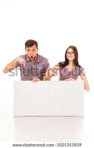 A guy and a girl are posing with a white sign in their hands. Isolated image. For advertising, logo, text. Emotional photo. Actor play.