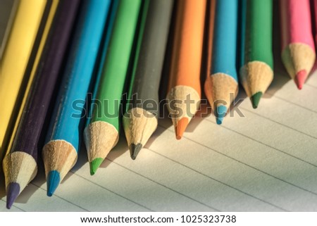 Shallow focus view of a close-up image of new colouring pencils seen on blank writing paper. Detail of some of the colouring pencil tips is evident, seen on a classroom desk.