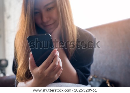 Closeup image of a beautiful Asian woman holding , using and looking at smart phone with feeling happy