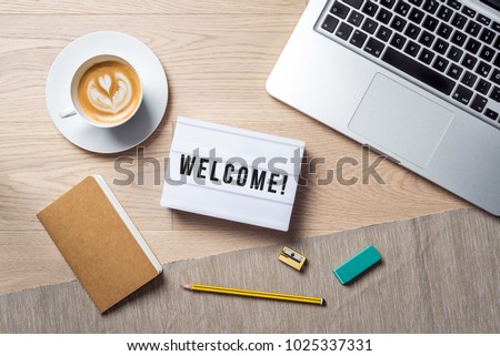 Welcome writing in lightbox lying on wooden desk with office supply and coffee cup as flat lay from bird's eye view