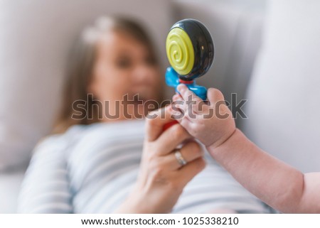 Mother play with baby with rattle. Family photo, lifestyle, focus on a toy. Beautiful mom holding her baby in arms with rattle. Portrait of a happy female and her toddler son playing with rattle