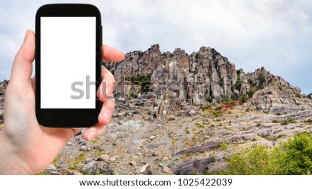 travel concept - tourist photographs old rocks at Demerdzhi (Demirci) Mountain from The Valley of Ghosts in Crimea in september on smartphone with cut out screen for advertising logo