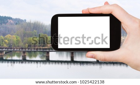 travel concept - tourist photographs Manshui Bridge on Yi river in Longmen Caves (Dragon's Gate Grottoes) area in China in spring season on smartphone with cut out screen for advertising logo