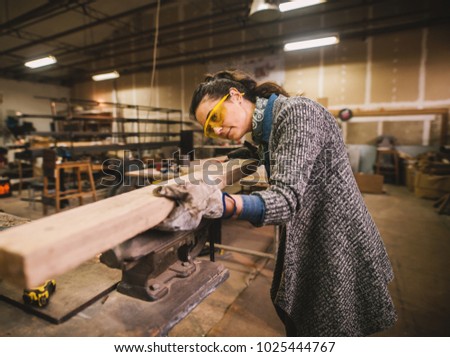 Portrait view of happy attractive hardworking middle aged professional female carpenter worker looking and choosing wood in the workshop or garage.