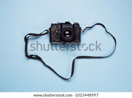 Minimal flat lay vintage camera with strap on a blue background, top view with copy space.