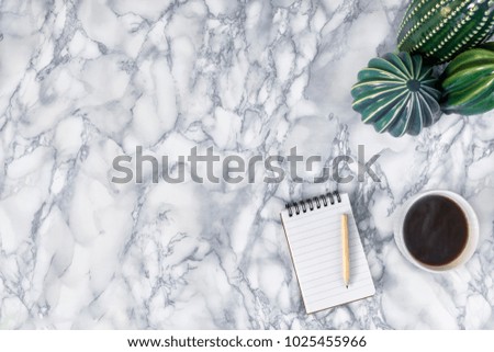 Marble desk seen from above with a notebook, pencil, pen, white cup of coffee and cactus