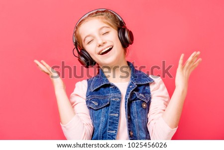 Cute young teen girl enjoying listening to music in wireless headset over rose background
