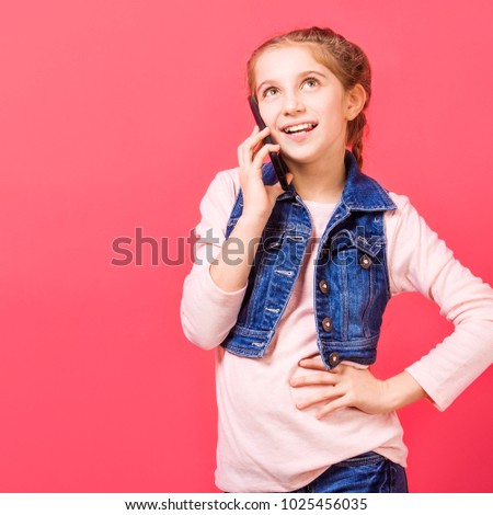 Young little girl speaking on the mobile phone while standing in front of pink background