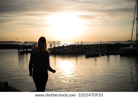 Girl standing on a balcony and watching the sunset over a port in germany?.