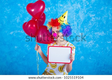 Happy clown. Concept of holidays. A cheerful young girl in a clown suit posing in front of a camera on a blue background. 1 April Fools' Day concept. Birthday.