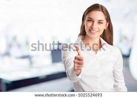 A beautiful young businesswoman with toothy smile giving thumbs up while standing at the office. 