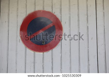 Close up view of a traffic sign indicating the interdiction of parking in front of a garage door. Wooden door made with white painted planks. Isoleted round red and blue symbol. Abstract street view.