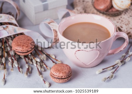 Pink coffee mug with sweet pastel french macaroons, gift box and pussy willow on light table from above. Breakfast on Mothers day or Women's day. Tender spring background.