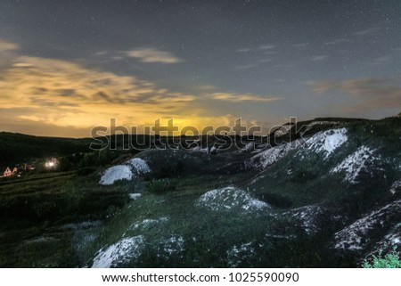 Night landscape with chalk ridges under cloudy and starry sky. White cretaceous hills at night. Natural archaeological monument - Krapivenskoye ancient settlement, Belgorod region, Russia.