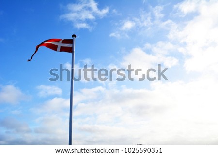 Danish flag blowing in the wind with several knots against the sky