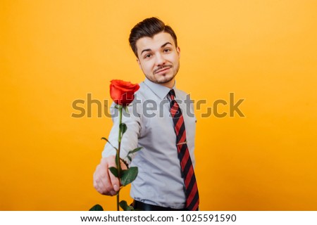 Cheerful handsome young man in casual giving a red rose.