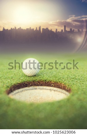 Picture of city by sunrise against golf ball at the edge of the hole