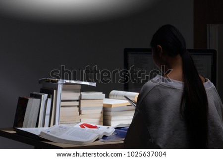 Asian Girl in white shirt reading many textbooks on table with many high stacking of international Books Journal Report, Woman works hard during night time, feel asleep tired, low exposure turn back