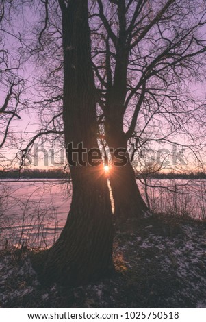 colorful winter sunset with light rays coming through the trees on the frozen river ice - vintage retro effect