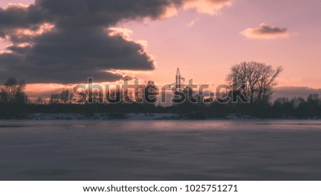 colorful winter sunset on frozen river ice with dramatic clouds - vintage retro effect