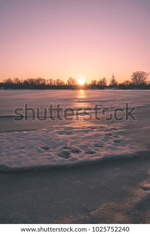 colorful winter sunset on frozen river ice with dramatic clouds - vintage retro effect