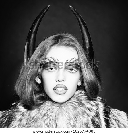 Closeup portrait of one beautiful wild young woman with bright golden animal monkey makeup with thorns on face and antlers in fur coat on black background, square picture