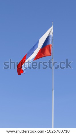 The national flag of Russia fluttering on a flagstaff against the background of the clear blue sky. State symbolics. Vertical format. Outdoors. Color. Photo.