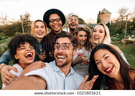 Friends chilling outside taking group selfie and smiling. Laughing young people standing together outdoors and taking selfie.