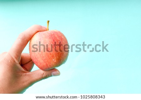 hand holding apple on blue background with copy space, healthy concept