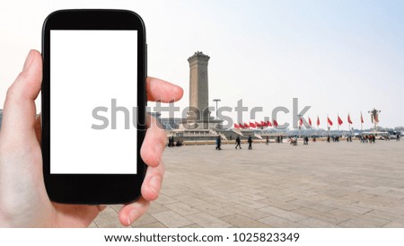 travel concept - tourist photographs the Monument of the People's Heroes on Tiananmen Square in Beijing city in China on smartphone with cut out screen for advertising logo