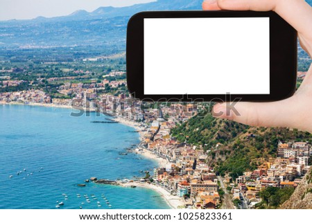 travel concept - tourist photographs Ionian sea shore with Giardini Naxos town in Sicily Italy in summer season on smartphone with cut out screen for advertising logo